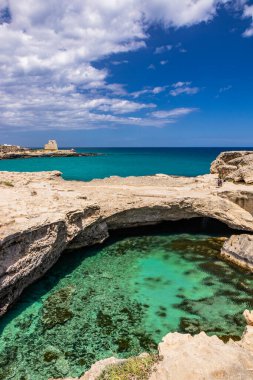 Roca Vecchia, Puglia, Salento, İtalya 'da arkeolojik alan ve turizm beldesi. Turkuaz deniz, berrak mavi gökyüzü, kayalar, güneş, yazın. Şiir Mağarası. Arka plandaki gözetleme kulesi..