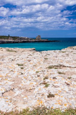 Roca Vecchia, Puglia, Salento, İtalya 'da arkeolojik alan ve turizm beldesi. Turkuaz deniz, berrak mavi gökyüzü, kayalar, güneş, yazın. 16. yüzyıl gözcü kulesi. Beyaz bulutlar ve güçlü rüzgar.