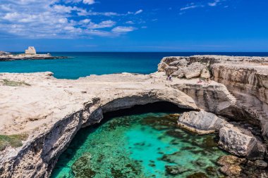 Roca Vecchia, Puglia, Salento, İtalya 'da arkeolojik alan ve turizm beldesi. Turkuaz deniz, berrak mavi gökyüzü, kayalar, güneş. Şiir Mağarası. Turistler güneşlenir. Arka plandaki gözetleme kulesi..