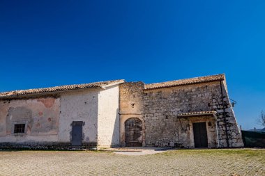 Ernici Dağları 'nda tuğla ve taştan yapılmış küçük bir kilise. Soyulmuş alçı, demir haç ve küçük bir çan. Collepardo 'da, Frosinone ili, Lazio, orta İtalya. Mavi gökyüzü ve parlak güneş.
