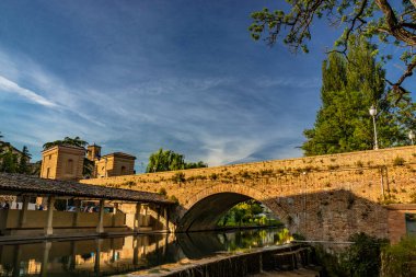 Bevagna 'nın ortaçağ köyünde, nehrin üzerindeki eski yıkama ve duvarcılık köprüsü. Perugia, Umbria, İtalya. Gün batımında mavi gökyüzü. Ağaçlar ve bitki örtüsü. Su yüzeyindeki yansıma..