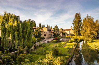 Eski ortaçağ köyü Bevagna 'yı geçen Chiasco Nehri. Perugia, Umbria, İtalya. Ağaçlar, bitki örtüsü, ekilmiş bahçeler. Yazın, gün batımında mavi gökyüzü.
