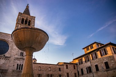 Ortaçağ 'ın Bevagna köyündeki San Michele Roma Kilisesi. Umbria, İtalya. Geniş bir gül penceresi ve Gotik çan kulesi olan Travertine cephesi. Mermer çeşme. Gün batımında