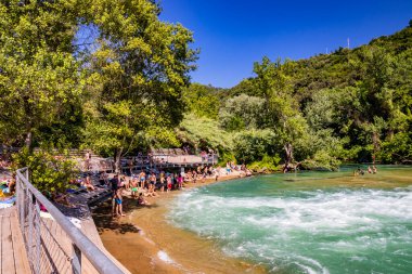 30 Haziran 2019 - Narni, Umbria, Terni, İtalya - Nera Nehri 'nin oluşturduğu küçük bir göl. Barajın açık kilidi güçlü bir su püskürtüsü gönderir. Turistler tehlikeyi umursamadan banyo yaparlar..