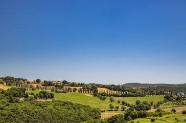 Umbria 'daki Amelia şehrinin tepesinden görülen yeşil Umbria tepeleri. Zengin bitki örtüsü, ekilmiş tarlalar, yazın açık mavi gökyüzü. Bir selvi bulvarı. Arkaplanda dağlar.