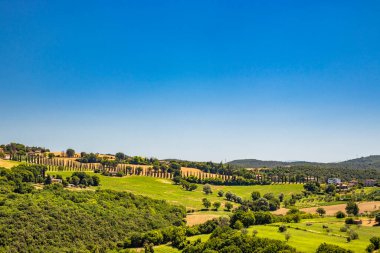 Umbria 'daki Amelia şehrinin tepesinden görülen yeşil Umbria tepeleri. Zengin bitki örtüsü, ekilmiş tarlalar, yazın açık mavi gökyüzü. Bir selvi bulvarı. Arkaplanda dağlar.