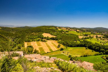Umbria 'daki Amelia şehrinin tepesinden görülen yeşil Umbria tepeleri. Zengin bitki örtüsü, ekilmiş tarlalar, yazın açık mavi gökyüzü. Bir selvi bulvarı. Arkaplanda dağlar.