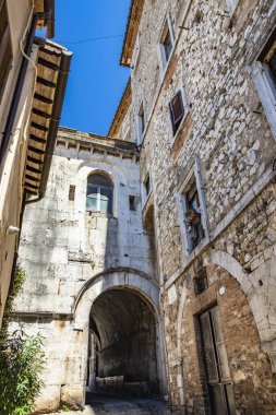 30 Haziran 2019 - Amelia, Umbria, Terni, İtalya - Şehrin karakteristik bir görüntüsü. Tarihi merkezdeki eski evlerin kaldırımlı sokağı, taş ve tuğla duvarları. Kemerli küçük bir galeri..