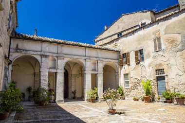 30 Haziran 2019, Amelia, Umbria, Terni, İtalya, şehrin merkezinde antik bir bina. Eski taş ve tuğla duvarlar, girişi, kolonları, kemerleri olan avlu. Saksılar dolusu çiçek..