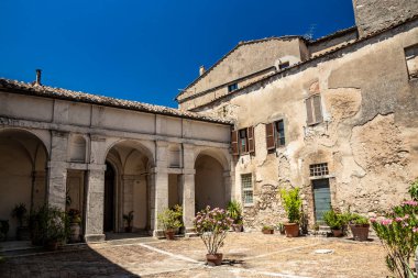 30 Haziran 2019, Amelia, Umbria, Terni, İtalya, şehrin merkezinde antik bir bina. Eski taş ve tuğla duvarlar, girişi, kolonları, kemerleri olan avlu. Saksılar dolusu çiçek..