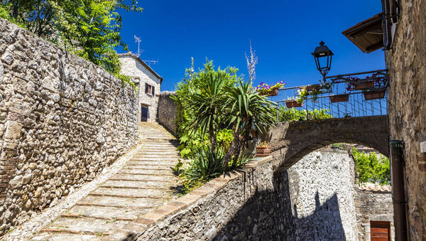 A characteristic glimpse of the city of Amelia, in Umbria. The cobbled alley, the stairs, the stone and brick walls of the old houses in the historic center. Plants and ornamental flowers.