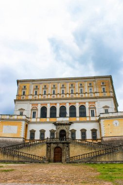 3 Haziran 2016 - Caprarola, Viterbo, Lazio, İtalya - Villa Farnese. Binanın dış cephesine bakın, merdivenler girişe çıkıyor. Bulutlu mavi gökyüzü. Duvardaki güneş saati ve saat..