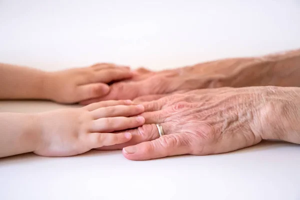 An elderly woman (old lady, grandmother) holds her little granddaughter\'s small hands. Family unity, love, help, assistance. Age and generational difference. Aged and wrinkled hands with young hands.