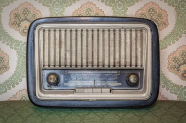 Elle ayarlamak için düğmeleri ve düğmeleri olan eski bir transistör telsizi. Arka planda eski bir duvar kağıdı var. Zaman tarafından yıpranmış ve yıpranmış eski bir nesne. Antikalar