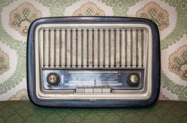 Elle ayarlamak için düğmeleri ve düğmeleri olan eski bir transistör telsizi. Arka planda eski bir duvar kağıdı var. Zaman tarafından yıpranmış ve yıpranmış eski bir nesne. Antikalar