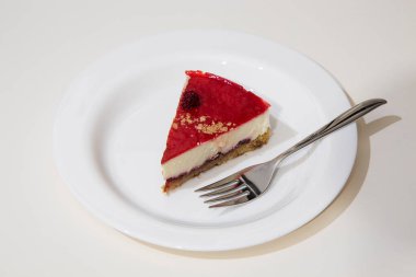 Beyaz tabakta bir dilim cheesecake, çelik pasta çatalı. Beyaz arkaplan.