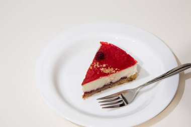 Beyaz tabakta bir dilim cheesecake, çelik pasta çatalı. Beyaz arkaplan.