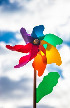 Ahşap çubuklu renkli bir Catherine tekerlek rüzgarı. Aşağıdan çekilen mavi gökyüzü ve arka planda bulutlar, rüzgarlı bir günde. Bir elin değneği tutuyor..