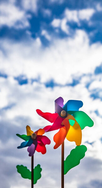 A colored Catherine wheel wind (pinwheel) with wooden stick. Shot from below with blue sky and clouds in the background, on a windy day.