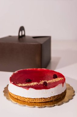 Bir peynirli keki paketinden çıkarmak. Böğürtlen ve ahududulu kırmızı reçelli cheesecake. Beyaz bir masada, kahverengi bir kutuda..