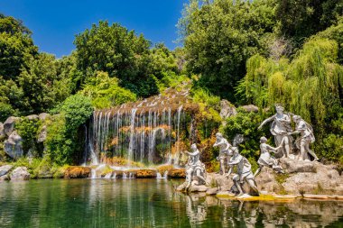 3 Temmuz 2020 - Caserta Kraliyet Sarayı - Mermer heykeller, şelale ve su manzaralı büyük çeşme. Yazın mavi gökyüzü. Ağaçlar ve zengin bitki örtüsü.