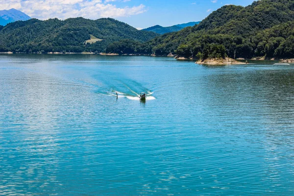 The lake of Salto, the largest artificial lake in Lazio, in the province of Rieti and created by damming the Salto river with the Salto dam. A sportsman practices water skiing towed by a motorboat.