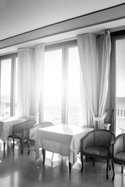Pencereden deniz manzarası harika olan bir otelin masaları. Bir yaz günü pencereden içeri ışık girer. Tatiller, rahatlama, lüks, huzur, sükunet, dinlenme.