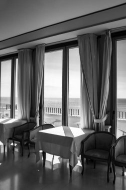 Pencereden deniz manzarası harika olan bir otelin masaları. Bir yaz günü pencereden içeri ışık girer. Tatiller, rahatlama, lüks, huzur, sükunet, dinlenme.