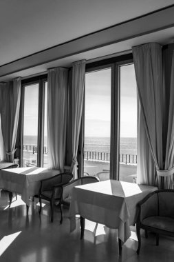 Pencereden deniz manzarası harika olan bir otelin masaları. Bir yaz günü pencereden içeri ışık girer. Tatiller, rahatlama, lüks, huzur, sükunet, dinlenme.