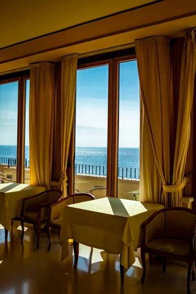 The tables of a hotel with a splendid view of the sea from the window. Light enters through the window on a summer day. Holidays, relaxation, luxury, peace, tranquility, rest.