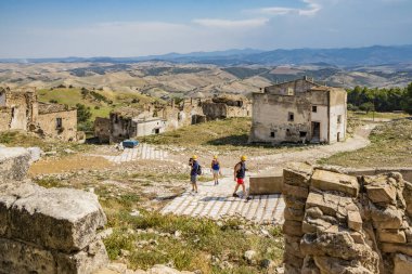 Craco, Basilicata, İtalya. Bir heyelan sonucu hayalet kasaba yok edildi ve terk edildi. Eski köyün kalıntıları ve kalıntıları görünüyor. Koruyucu kask takan bazı turistler kenti ziyaret ediyor