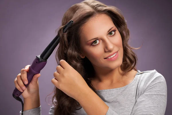 Beautiful woman using curling iron on her shiny hair, beauty and hairstyle