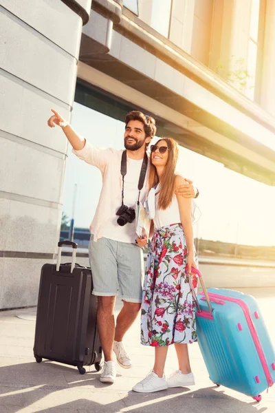 young couple with luggage walking on footpath against sunny sky