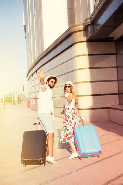 Beautiful young couple with luggage and straw hats says goodbye on airport, going to summer vacation