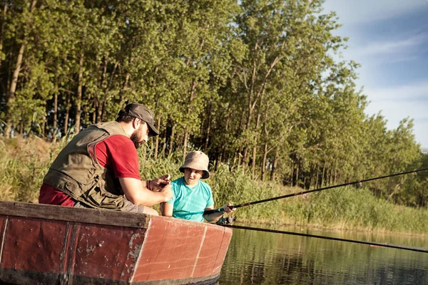 father and son fishing together with rods on wooden boat at lake