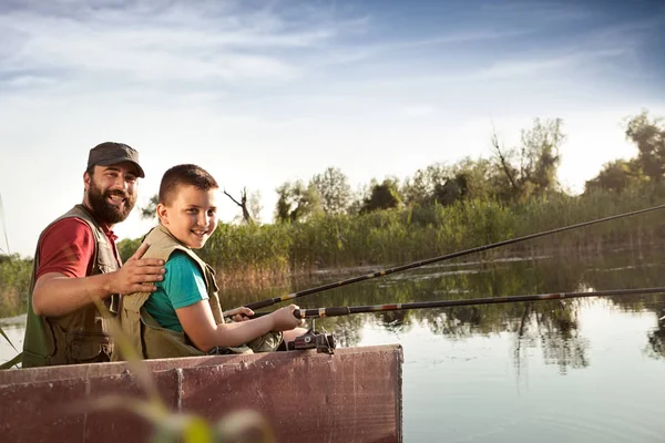 Dad and son fishing from wooden boat on river, happy family together in nature