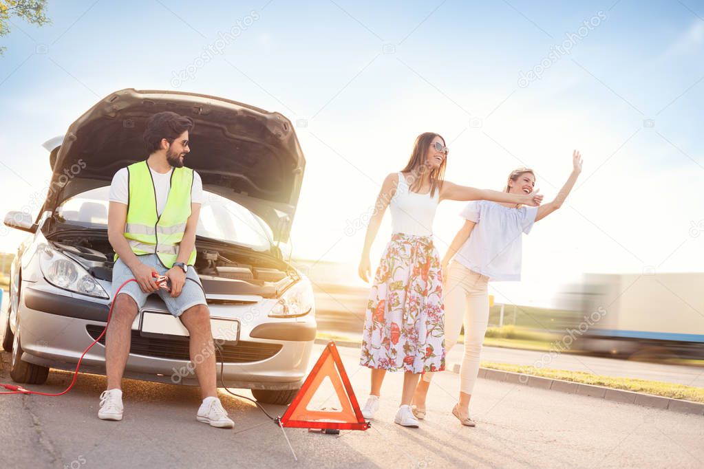 young man next to the broken car leaves his female friends to hitchhiking for help