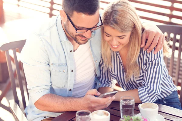 Beautiful couple having coffee on a date, having fun together with smartphone