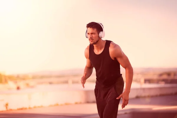 Attractive fit man running fast along bridge at sunset light, man doing workout outdoor, runner with amazing sunset on background