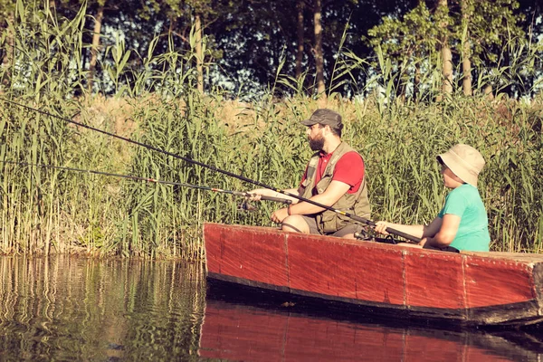 Father and son fishing from wooden boat in river, common hobby, vacation and holiday, family lifestyle