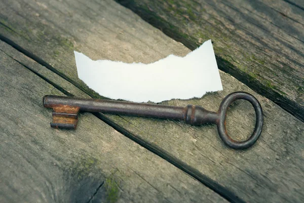 Old door key and white ripped piece of paper on old planks