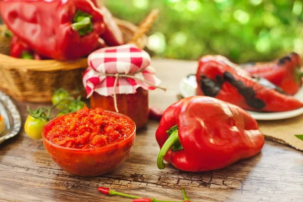 Ajvar in glass bowl with roasted pepper on the table