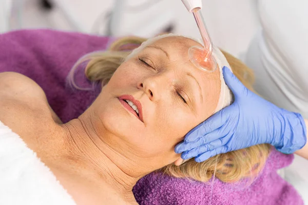 Donna in cappello cosmetico riceve darsonvalizzazione trattamento viso — Foto Stock
