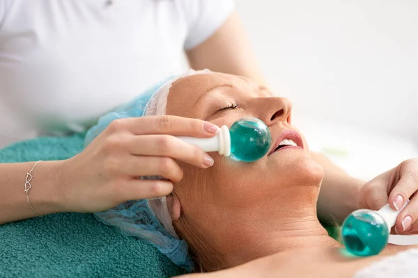 Mujer mayor recibiendo masaje facial con bolas de vidrio frío —  Fotos de Stock