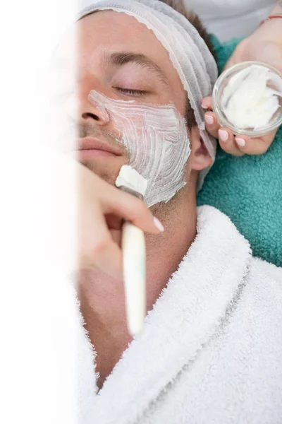 Beautician applying cream on male face with a brush