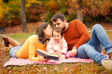 Her zaman çocuğumuzu taşır. Parkta çimenlerin üzerinde otururken gülümseyen üç mutlu genç aile