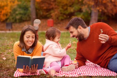 Anne, baba ve kızı çimenlerin üzerinde vakit geçiriyorlar. 