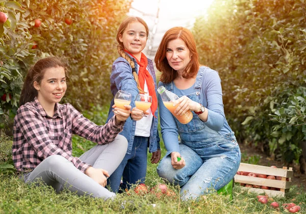 若い女性は 自然有機ジュースとボトルを保持しています 晴れた日に庭から生産 眼鏡フルジュースとブロンドの女の子の隣に — ストック写真