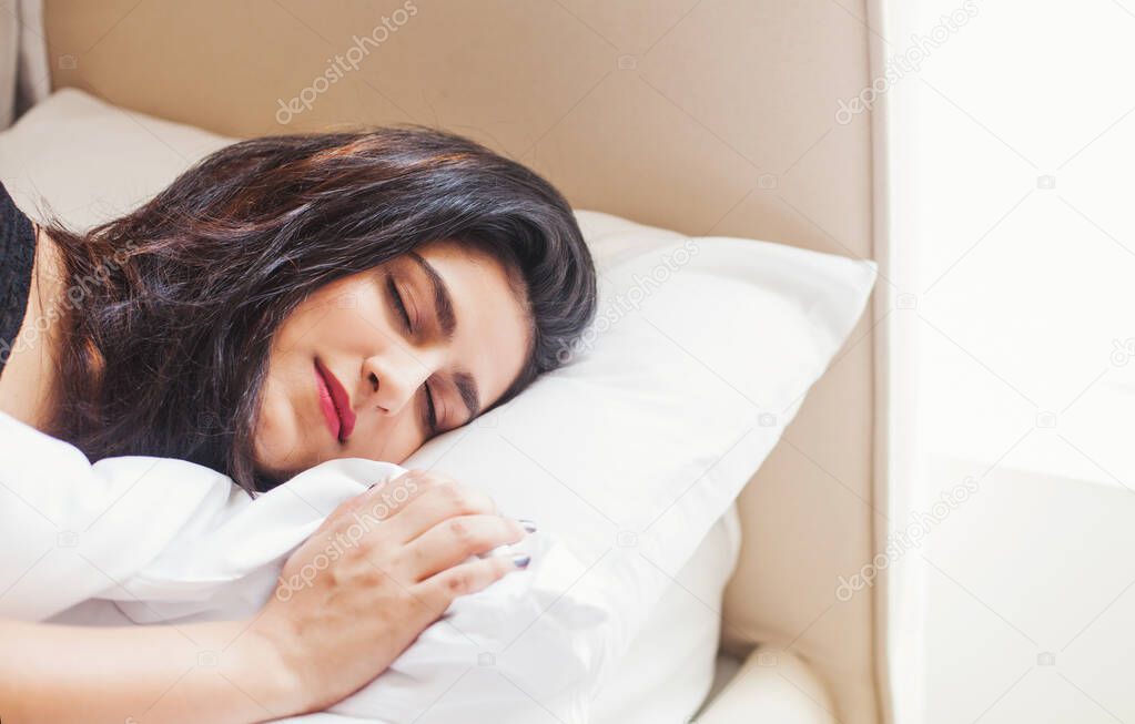 Beautiful Indian woman sleeping in a daytime in a cozy bed, closeup portrait