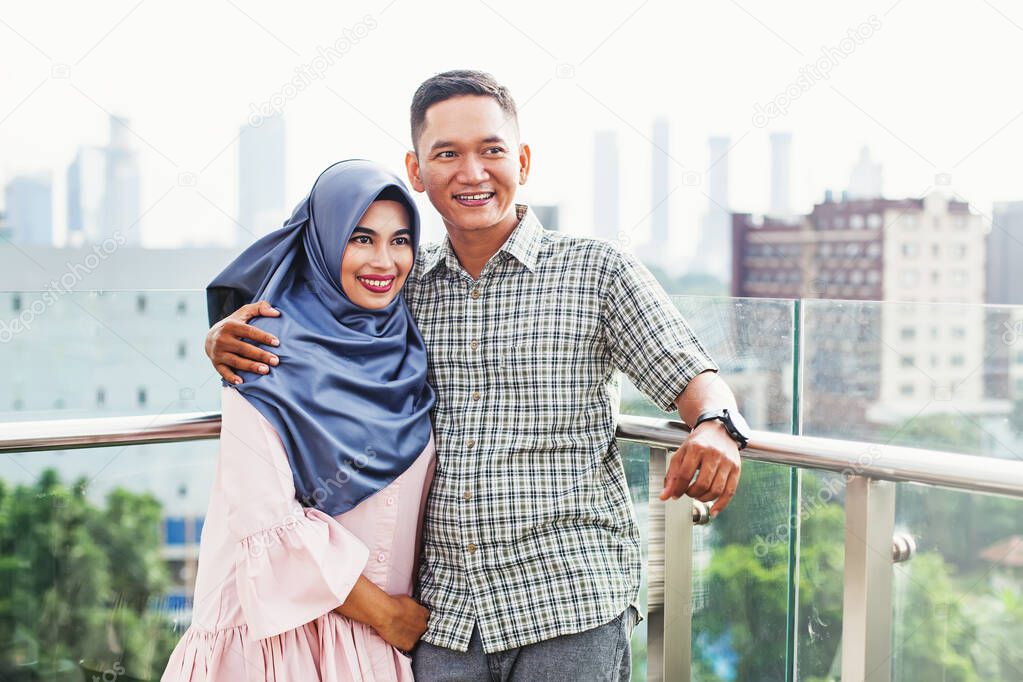 Happy Indonesian couple hugging on a balcony over Jakarta city v